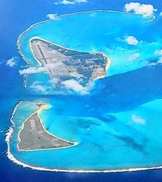 an island in the middle of blue water with clouds around it and two smaller islands on each side