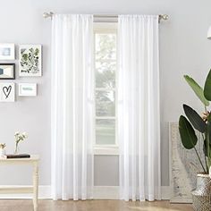 a living room with white curtains and pictures on the wall above it, along with a plant in a vase