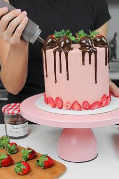 a woman is decorating a cake with chocolate and strawberries