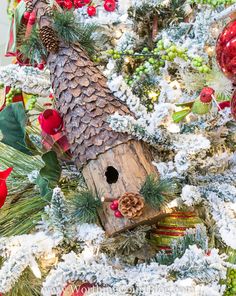 a birdhouse is sitting in the middle of a christmas tree with pine cones and berries