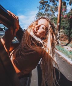 a woman with long blonde hair is sitting in the back seat of a car and smiling