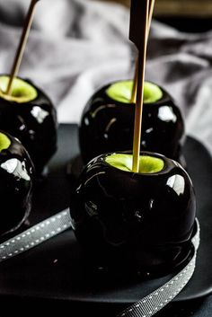 an image of some black apples on a plate with toothpicks sticking out of them