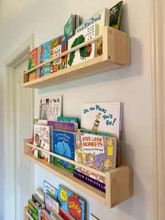 two wooden shelves filled with children's books on top of a white wall next to a doorway