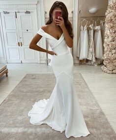 a woman in a white dress taking a selfie with her cell phone while wearing a wedding gown