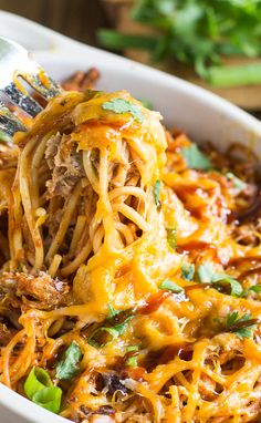 a fork full of spaghetti being lifted from a casserole dish with meat and cheese