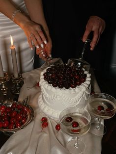 a bride and groom cutting their wedding cake with cherries on the table in front of them