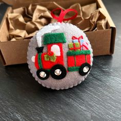 a christmas ornament with a train on the front in a gift box next to it