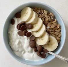 a blue bowl filled with granola, bananas and chocolate chips next to a spoon