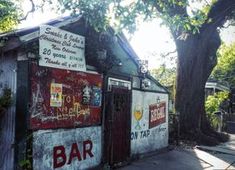 an old bar with graffiti on the side of it's wall next to a tree