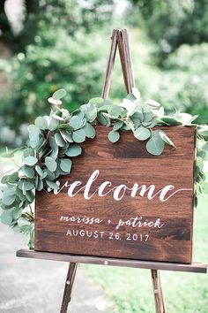 a wooden welcome sign with greenery hanging from it's sides on a easel