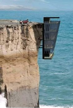 a cliff face with a glass window on the top and ocean in the back ground