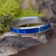 a blue ring sitting on top of a piece of wood next to some rocks and moss