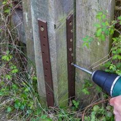 a person is using a drill to fix a fence post in the grass and weeds