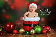 a baby wearing a santa hat sitting in a bucket surrounded by christmas ornaments