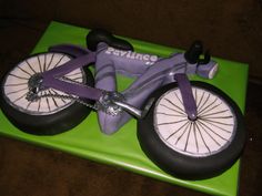 a cake shaped to look like a bicycle on a green mat with the words raviings written on it