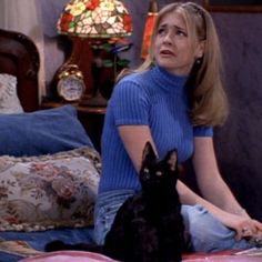 a woman sitting on top of a bed with a black cat in front of her