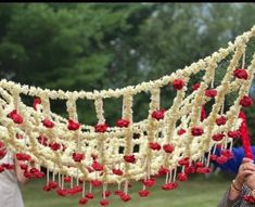 a woman holding up a red and white string with flowers hanging from it's sides