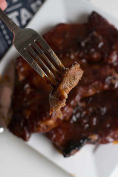 a fork is holding up some meat with sauce on the top and ribs in the bottom