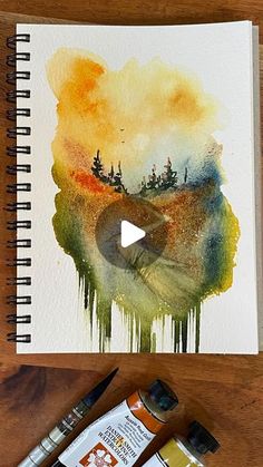 an art project with watercolors and paintbrushes on a wooden table next to it