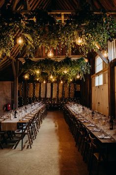 the long tables are set up for an event with greenery hanging from the ceiling