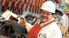 a man wearing a white hard hat and an orange apron is working in a hot dog shop