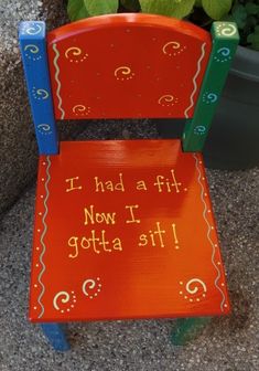 a wooden chair with writing on it sitting next to a potted plant