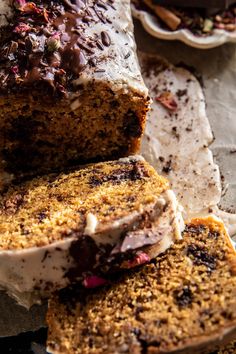 a loaf of cake with frosting and chocolate toppings on top, sitting next to another loaf of cake