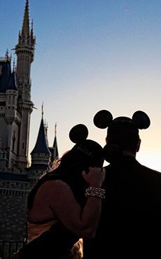 a man and woman standing in front of a castle with mickey mouse ears on their heads