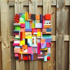 a colorful piece of art made out of different colored papers on a wooden board fence