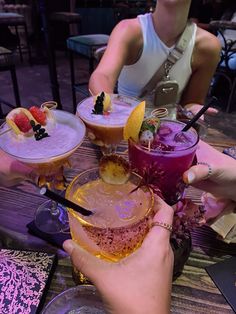 several people are holding up glasses with different drinks in them on a table at a restaurant