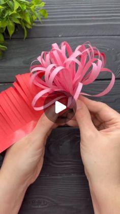 someone is making a paper flower out of red construction paper and some pink ribbon on top of it