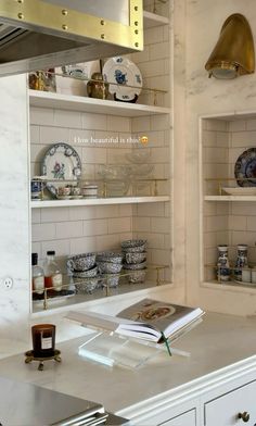 a kitchen with white cabinets and shelves filled with plates, cups and saucers on top of them