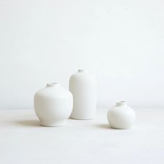 three white vases sitting next to each other on top of a table in front of a white wall