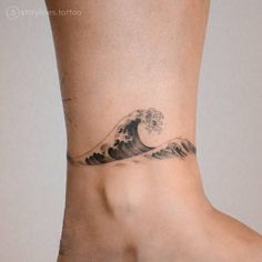 a woman's foot with a wave tattoo on the side of her leg and an ocean wave behind it