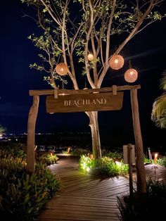 a wooden walkway leading to a sign that says beach and lights are on the trees