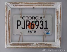 an old white framed license plate hanging on a wall in a frame with twine strings