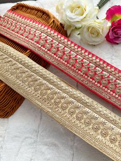 two gold and red belts sitting on top of a white blanket next to flowers in a basket