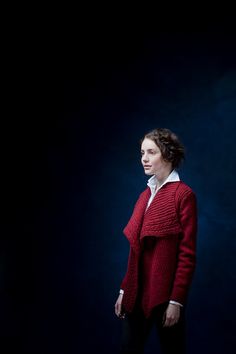 a woman in a red sweater and black pants poses for a photo against a dark background