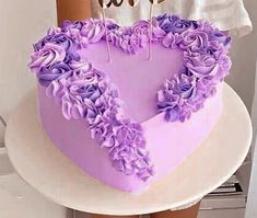 a heart - shaped cake with purple flowers on the bottom is being held by a woman