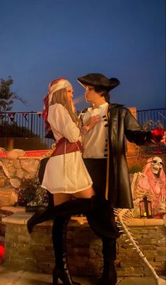 a man and woman dressed up in pirate costumes standing next to each other on a stone wall