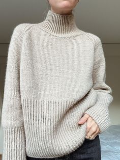 a woman standing in front of a bed wearing a turtle neck sweater