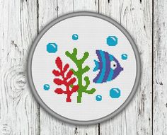 a cross stitch fish and seaweed pattern on a white wooden background with grey frame