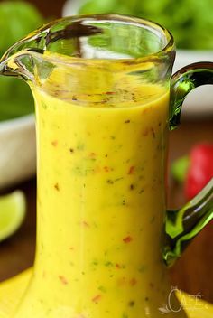 a glass pitcher filled with yellow liquid sitting on top of a wooden table next to vegetables