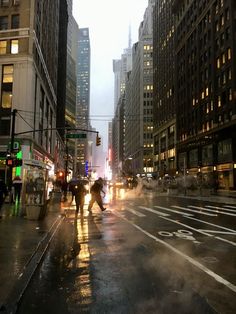 people crossing the street at an intersection on a rainy day with buildings in the background