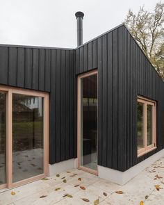 a black building with two windows and some leaves on the ground