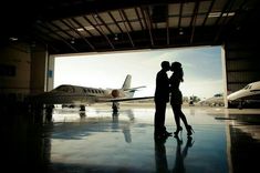 a man and woman standing in front of an airport hangar with a plane parked behind them