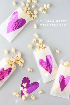 three bags filled with hearts and popcorn on top of a white table next to purple paper