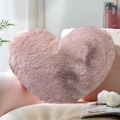 a pink heart shaped pillow sitting on top of a couch next to a white rose