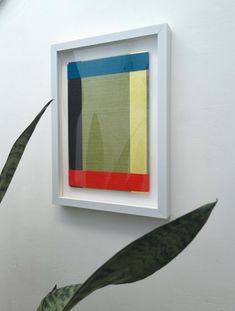 an abstract painting hangs on the wall next to a plant in a white square frame