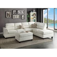 a living room with a white sectional couch and ottoman in front of a large window